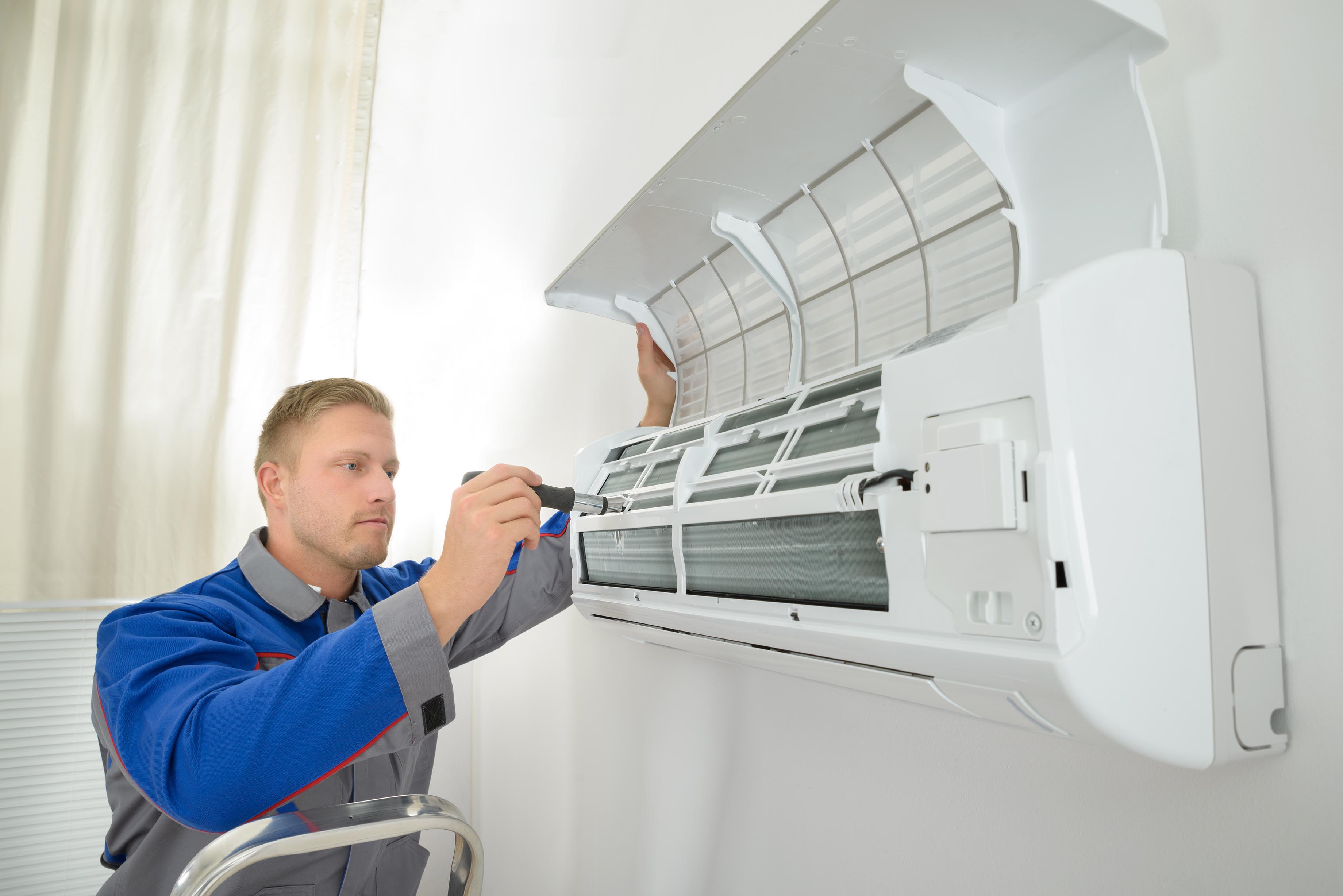 Young Man Repairing Air Conditioner Standing On Stepladder